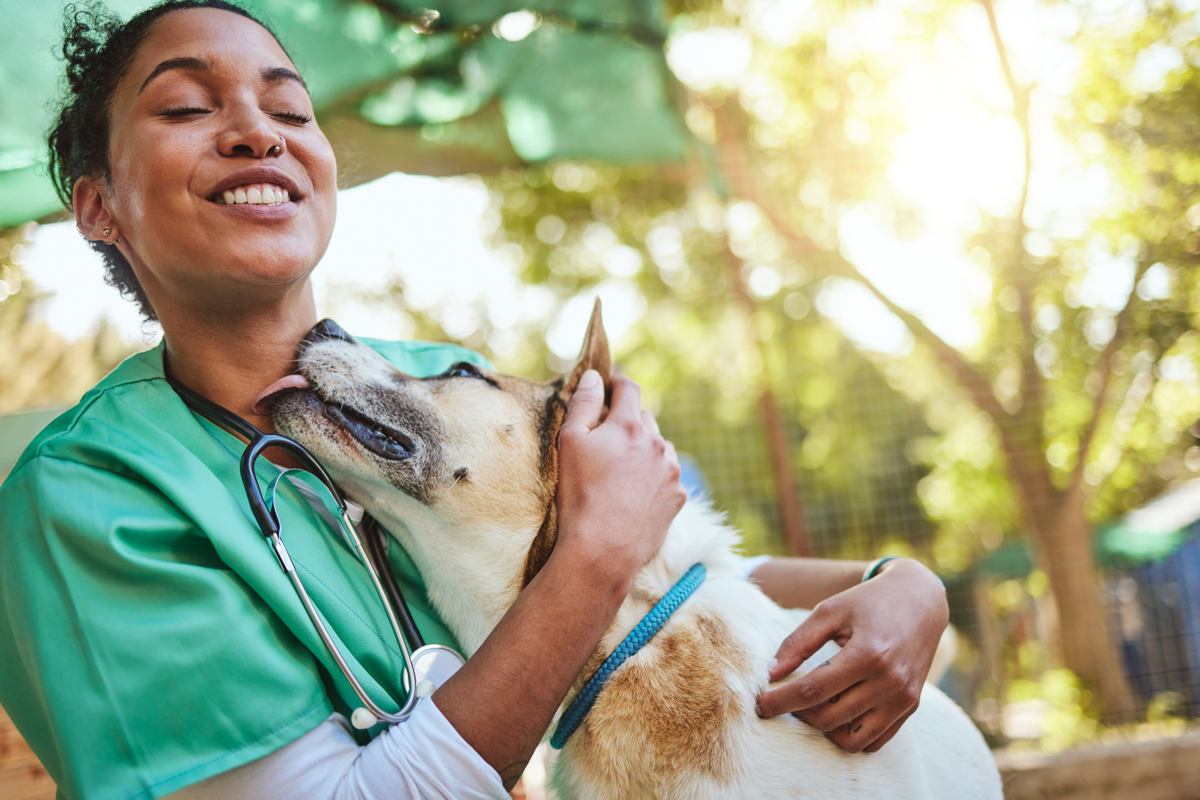 Vet Hugging Dog Smiling veterinarian in green uniform hugging happy dog outdoors