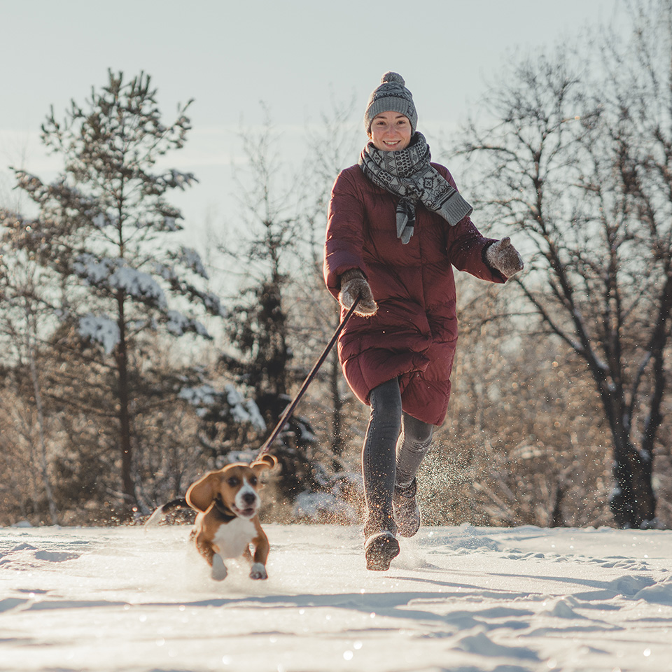 A woman running with her dog in the snow, both enjoying the winter weather.