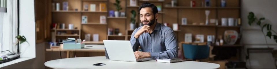 A man sitting at a table with a laptop, working on his computer.