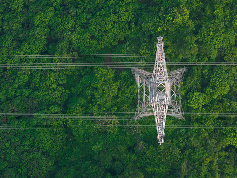 An electricity tower stands tall amidst a lush green forest in this aerial view.